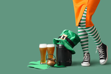 Female legs in stockings with glasses of beer, barrel and leprechaun's hat on green background. St....