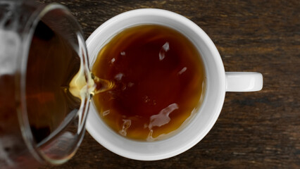 Pouring black tea in white cup, top view