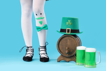 Female legs with funny face, glasses of beer, barrel and leprechaun's hat on blue background. St....
