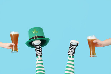 Female legs in green stockings with leprechaun's hat and glasses of beer on blue background. St....