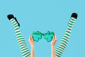 Female legs in green stockings with clover shaped novelty glasses on blue background. St. Patrick's...