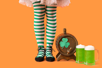 Woman in waitress costume with barrel and glasses of beer on orange background. St. Patrick's Day...