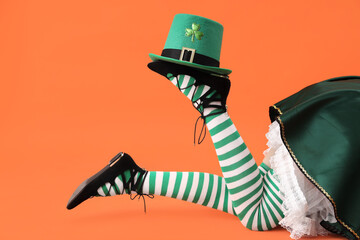 Woman in waitress costume with leprechaun's hat on orange background. St. Patrick's Day celebration