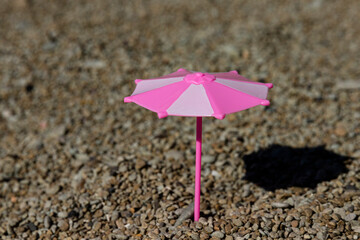 Toy umbrella with a shadow from the sun on a rocky beach, seashore. The concept of a place under the sun.