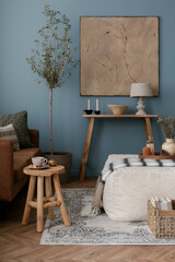 Interior design of rural style living room with white armchair, wooden shelf, olive tree, paintings, decorations and elegant accessories. Template. Blue wall. 