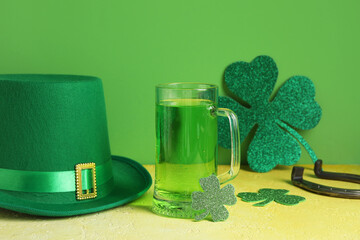 Mug of green beer with leprechaun hat, horseshoe and paper clovers on yellow grunge table against...