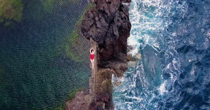 A beautiful overhead drone shot of a naturally formed lava pool in Porto Moniz, Madeira. A beautiful girl in a swimsuit swims among the waves in a lava pool.