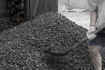 A worker with a shovel unloads black coal against the background of a large pile of coal. Energy...