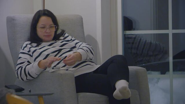 Pregnant woman relaxing on chair at home doing glucose level blood test, indoor, evening