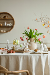 Creative composition of spring easter dining room interior with round table, vase with tulips,...