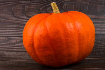 Orange pumpkin with a stem, close-up on a plank, wooden background. Autumn background. Copy space.
