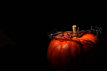 Orange pumpkin with a wreath of barbed wire, a crown of thorns, on a black background. Halloween...