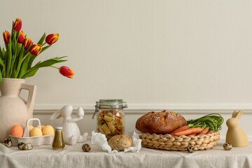 Creative composition of easter living room interior with bread, basket, carrot, vase with spring...