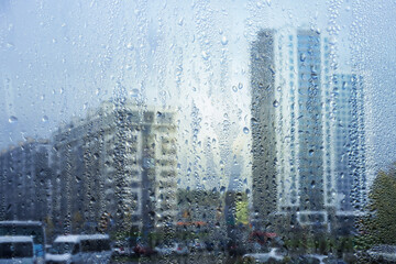 Rainy window, raindrops on the glass, against the background of a city street with houses and a road. Soft blurred background.