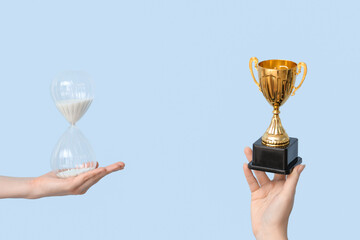 Female hands holding hourglass and gold cup on blue background