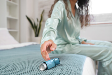 Young woman taking asthma inhaler from bed in bedroom, closeup - obrazy, fototapety, plakaty