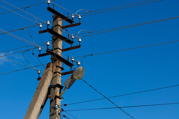 An electric pole with wires and a street lighting lamp against the blue sky during the day.