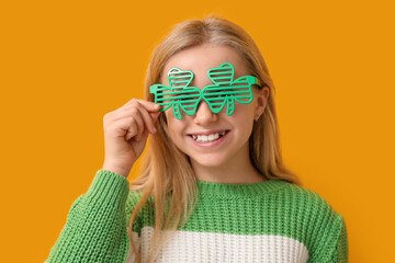Cute little girl in decorative glasses in shape of clover on yellow background. St. Patrick's Day...