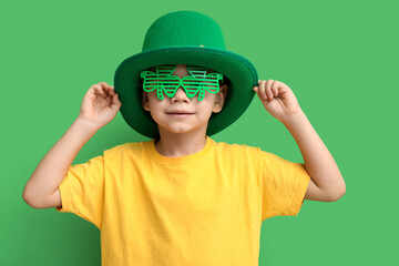 Cute little boy in leprechaun hat and decorative glasses in shape of clover on green background....