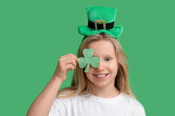 Cute little girl in leprechaun hat with clover on green background. St. Patrick's Day celebration