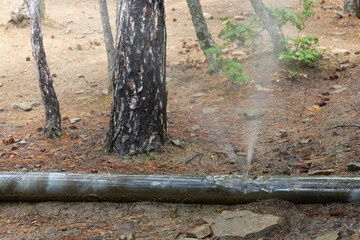Leakage of drinking water from a damaged water pipe in a mountainous area. Spray and a jet of water under pressure escape from the pipe.