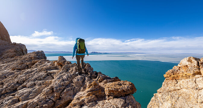 Woman hiker walking on mountain top cliff ege at lakeside