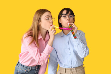 Beautiful young women with party whistles on yellow background. April Fools Day celebration