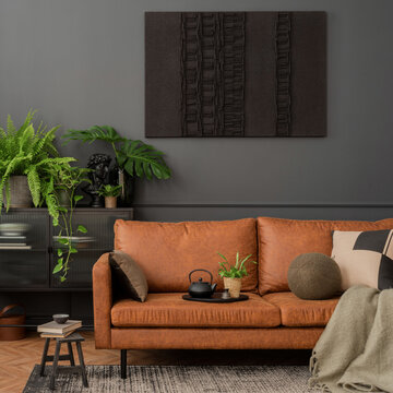 Interior design of living room interior with mock up poster frame, brown sofa, plants,  glass sideboard, stool, wooden floor, lamp and personal accessories. Home decor. Template.