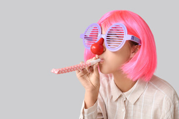 Beautiful young woman in funny disguise with party whistle on grey background. April Fools Day...