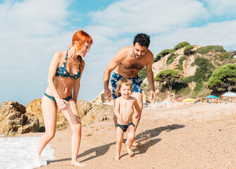 Cheerful couple walking on seashore playing with kid