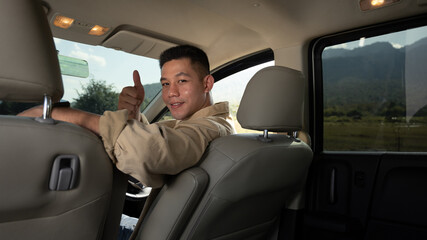 Happy young handsome man sitting inside car and showing thumbs up. Travel and active lifestyle concept
