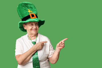 Senior woman in leprechaun hat pointing at something on green background. St. Patrick's Day...