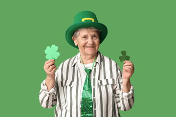 Senior woman in leprechaun hat with clover on green background. St. Patrick's Day celebration