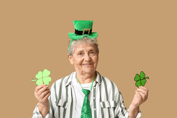 Senior woman in leprechaun hat with clover on brown background. St. Patrick's Day celebration