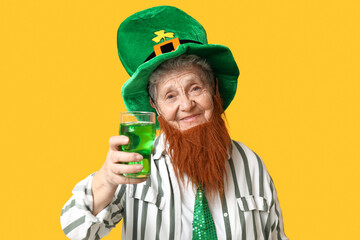 Senior woman in leprechaun hat with red beard holding glass of beer on yellow background. St....