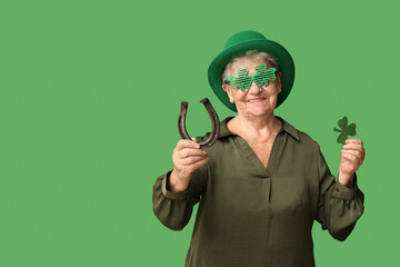 Senior woman in leprechaun hat with horseshoe and clover on green background. St. Patrick's Day...
