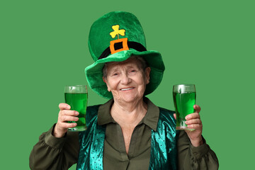 Senior woman in leprechaun hat with glasses of beer on green background. St. Patrick's Day...