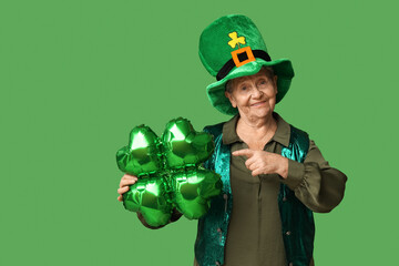 Senior woman in leprechaun hat pointing at air balloon in shape of clover on green background. St....