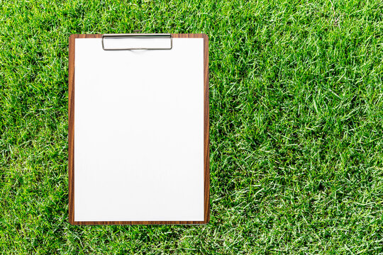 Blank white papaer on wooden clipboard with space on green grass background, education concept, outdoor day light