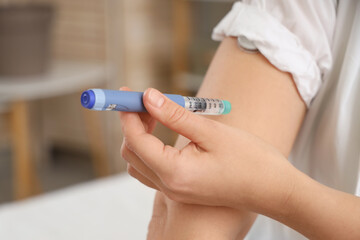 Diabetic woman using lancet pen in bedroom, closeup