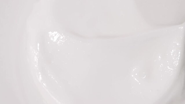 A jar of white moisturizing cosmetic cream rotates in different directions, top view.