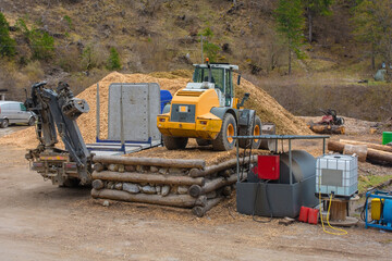 A flatbed container truck with a pneumatic lifting arm and a front end loader tractor at a saw mill...