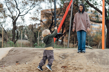 Little boy riding on a makeshift swing in the park . Mom looks at the flight of a little son.