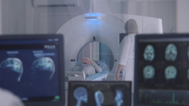 Professional female doctor controls MRI or CT or PET scan with patient undergoing procedure. Camera changes view to monitors with displayed brain scans results in control room. Healthcare Service.