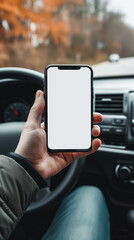 Smartphone blank screen mock up in driver's hand in front of the car steering wheel, selective focus. Mobile phone with isolated white screen. Navigate or GPS concept.