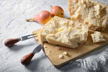 Parmigiano, Parmesan cheese. Grana with knife and fork for hard cheeses on wooden cutting board, close-up.