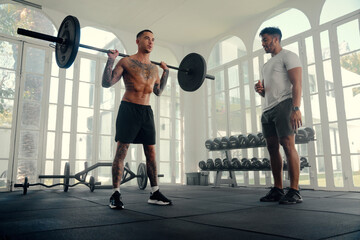 Two athletic multiracial young men in sports clothing doing weightlifting at the gym