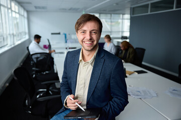 Happy young businessman in businesswear sitting on desk with digital tablet and digitized pen in...