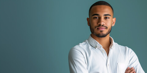 Confident young adult with a neatly trimmed beard, wearing a crisp white shirt against a teal background