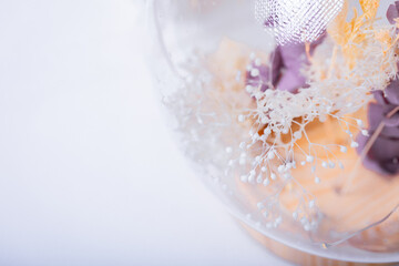 Enclosed bohemian miniature blooms housed within a glass orb atop a pristine white surface....